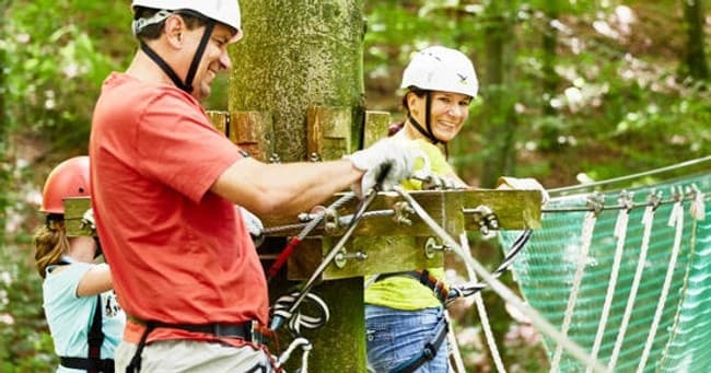Instructors securing harnesses for participants on wooded ropes platform