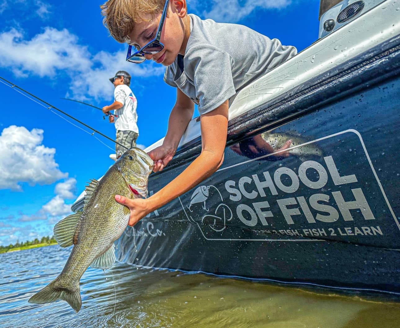 Boy releasing a bass beside a School of Fish boat on flats