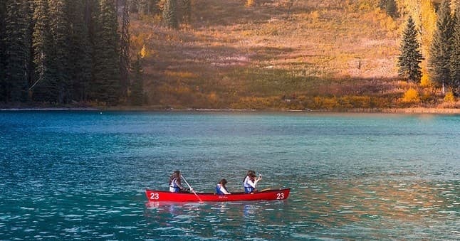 Canoeists paddling on alpine lake with autumn forest backdrop