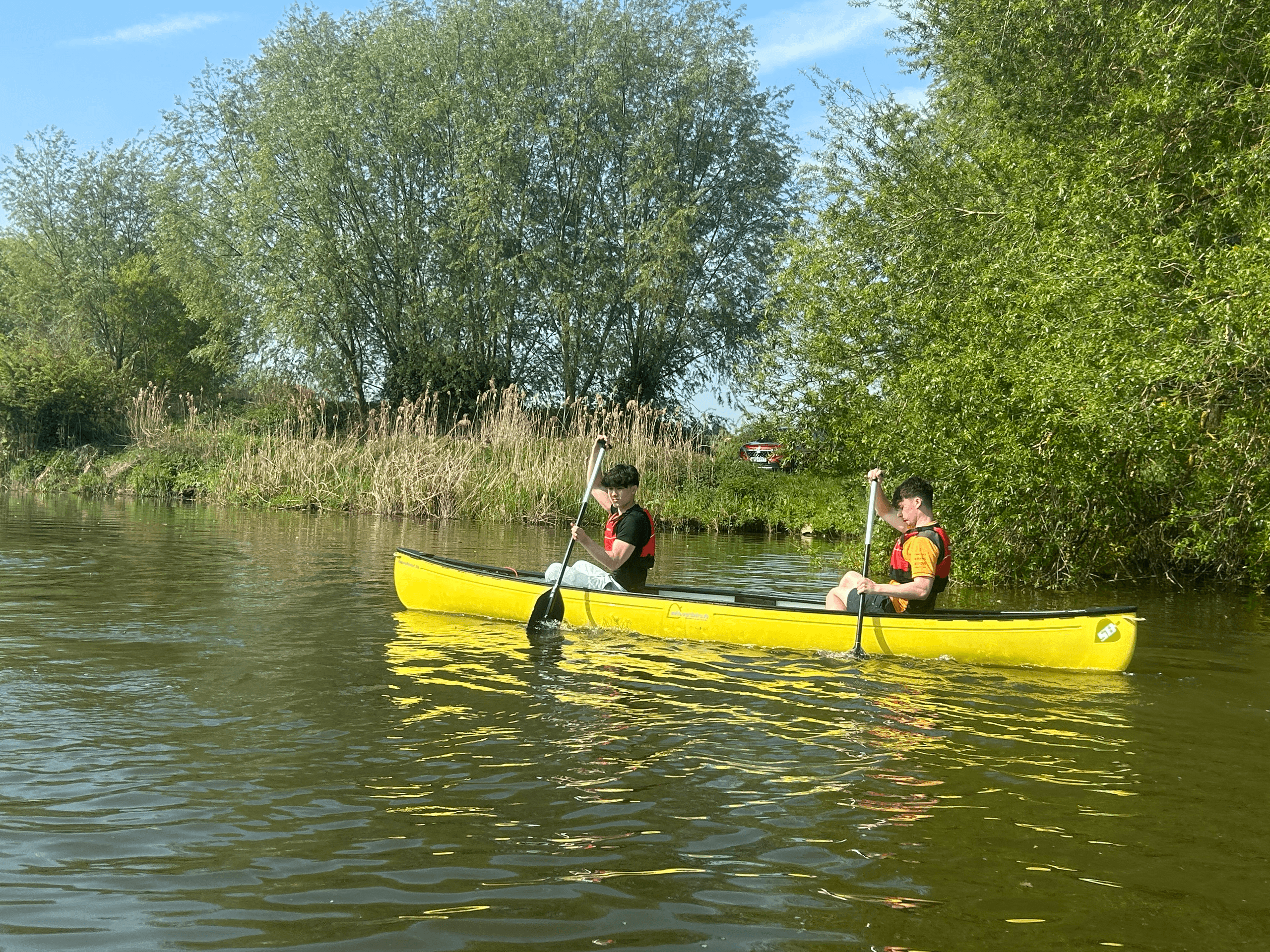 Canoeists paddling a tranquil river with willow-lined banks