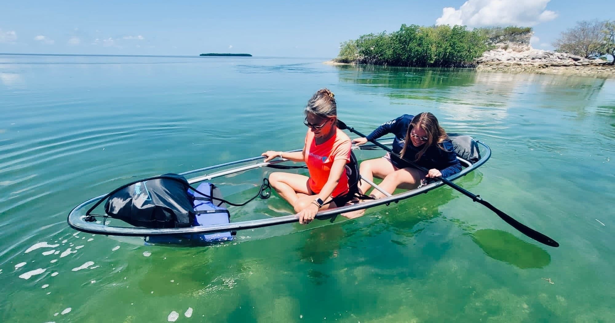 Two paddlers in clear kayak over turquoise shallow flats
