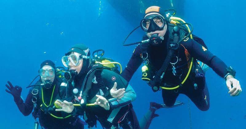 Three scuba divers cruising over bright blue Caribbean sea reef