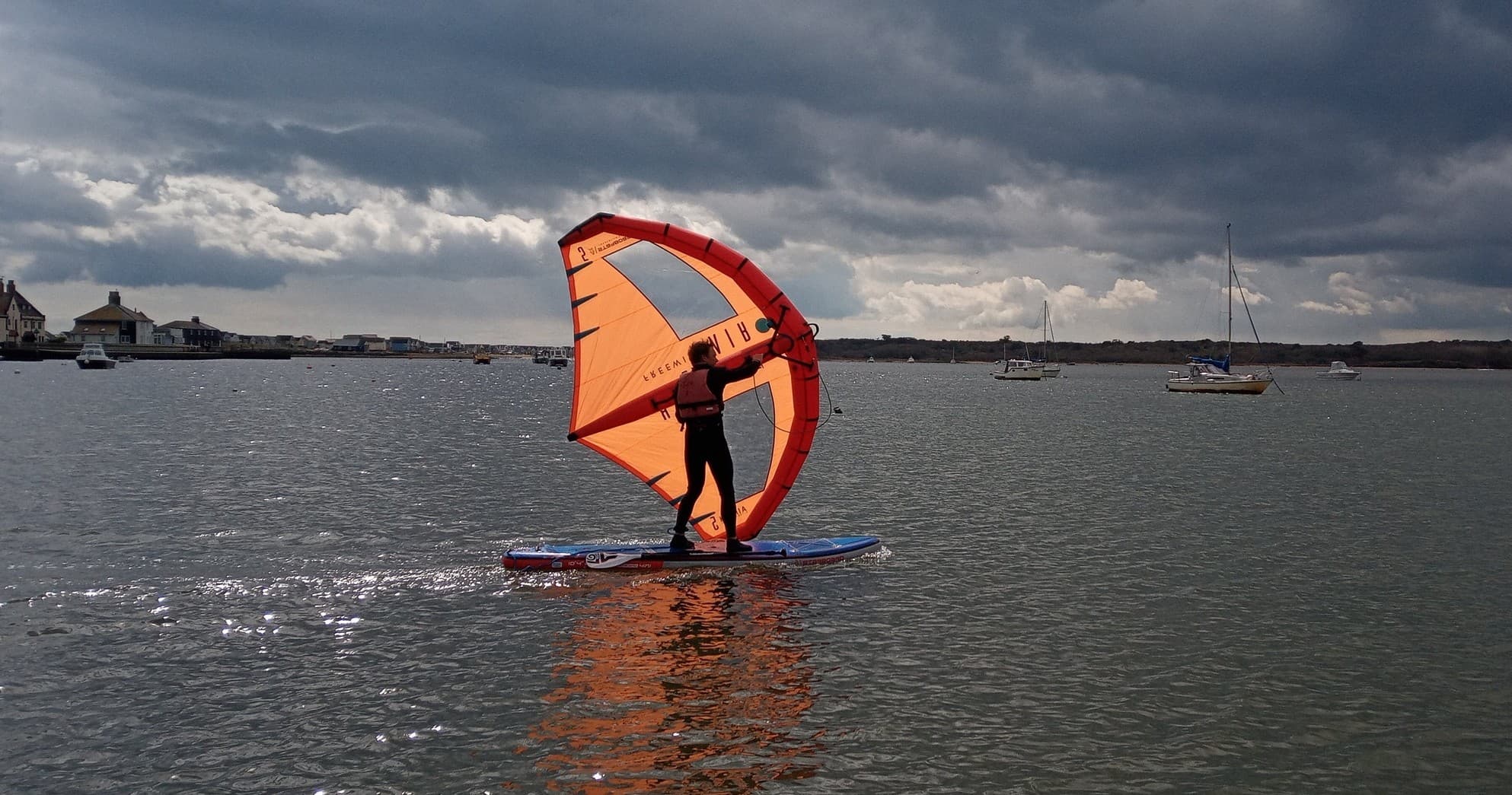 Windsurfer with orange wing riding coastal bay waves, action