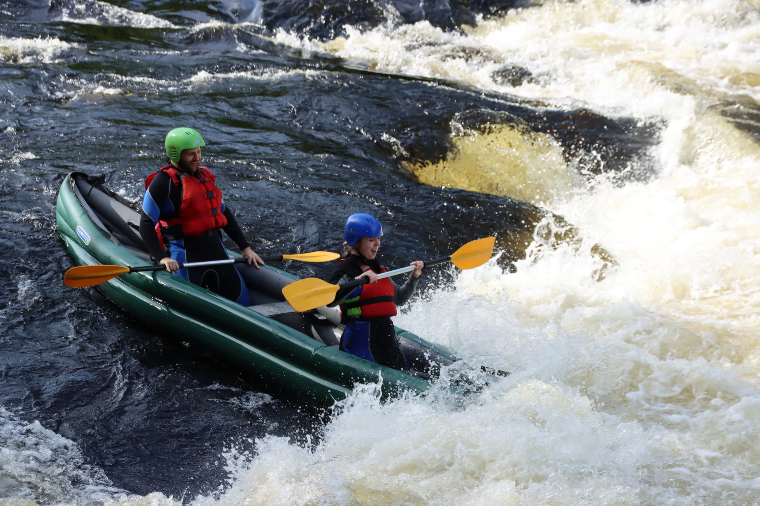 Two paddlers steering inflatable raft through fast river rapids