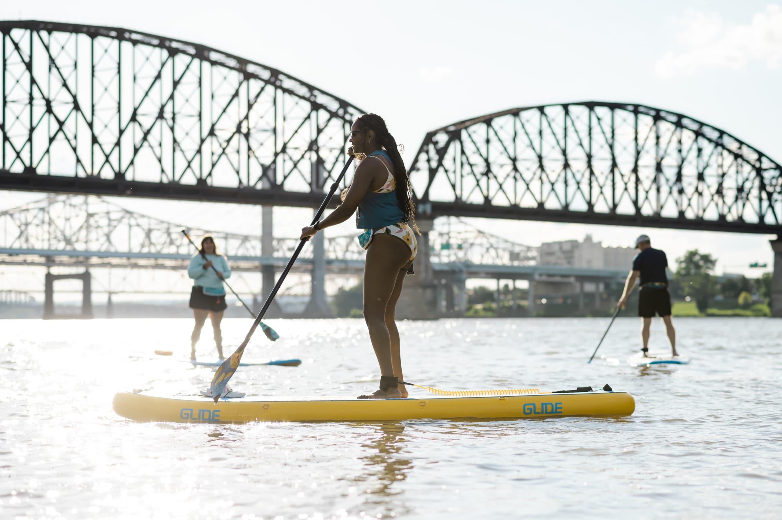 Stand-up paddleboarding group crossing river with bridge scenery