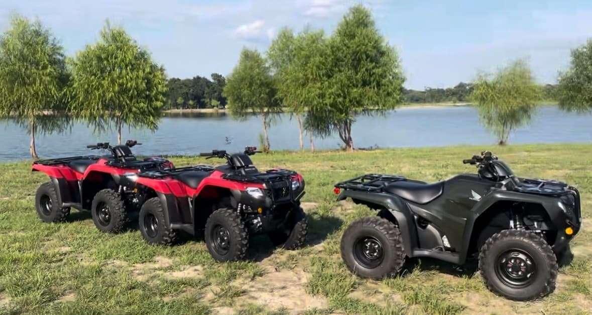 Red and black ATVs parked by lakefront grassy park ready for riding