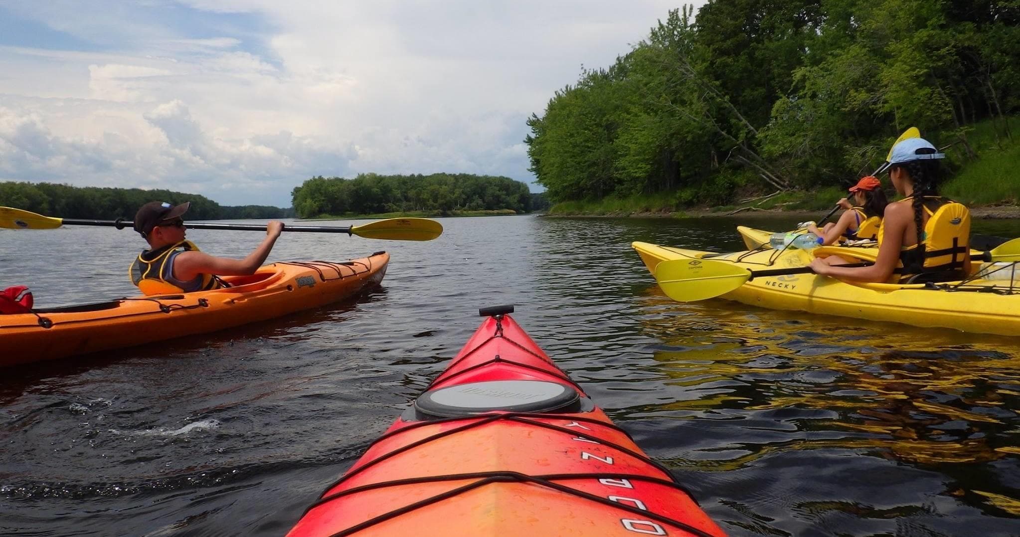 Kayaker's POV paddling with group on river through woods