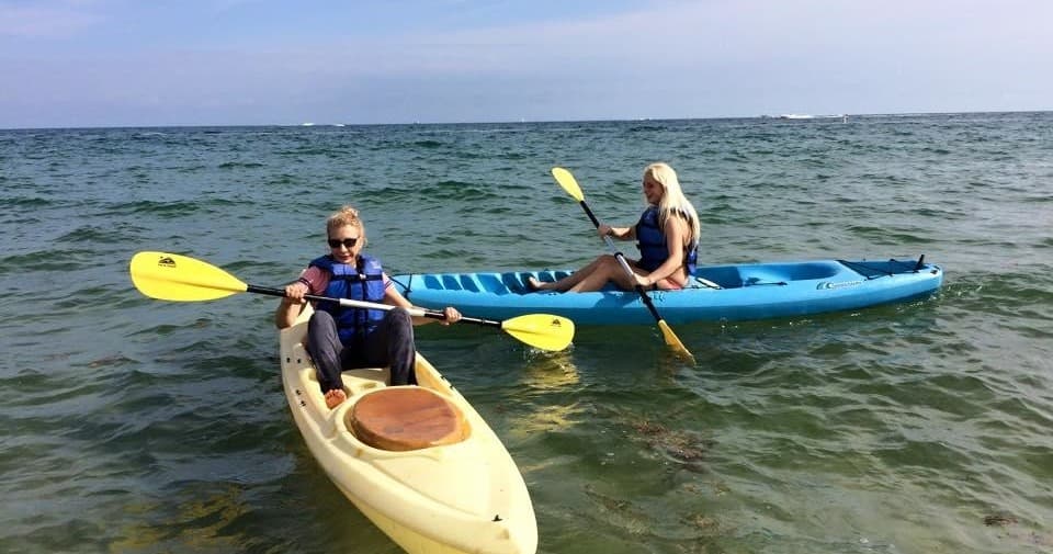 Two kayakers paddling near shore in shallow green ocean water