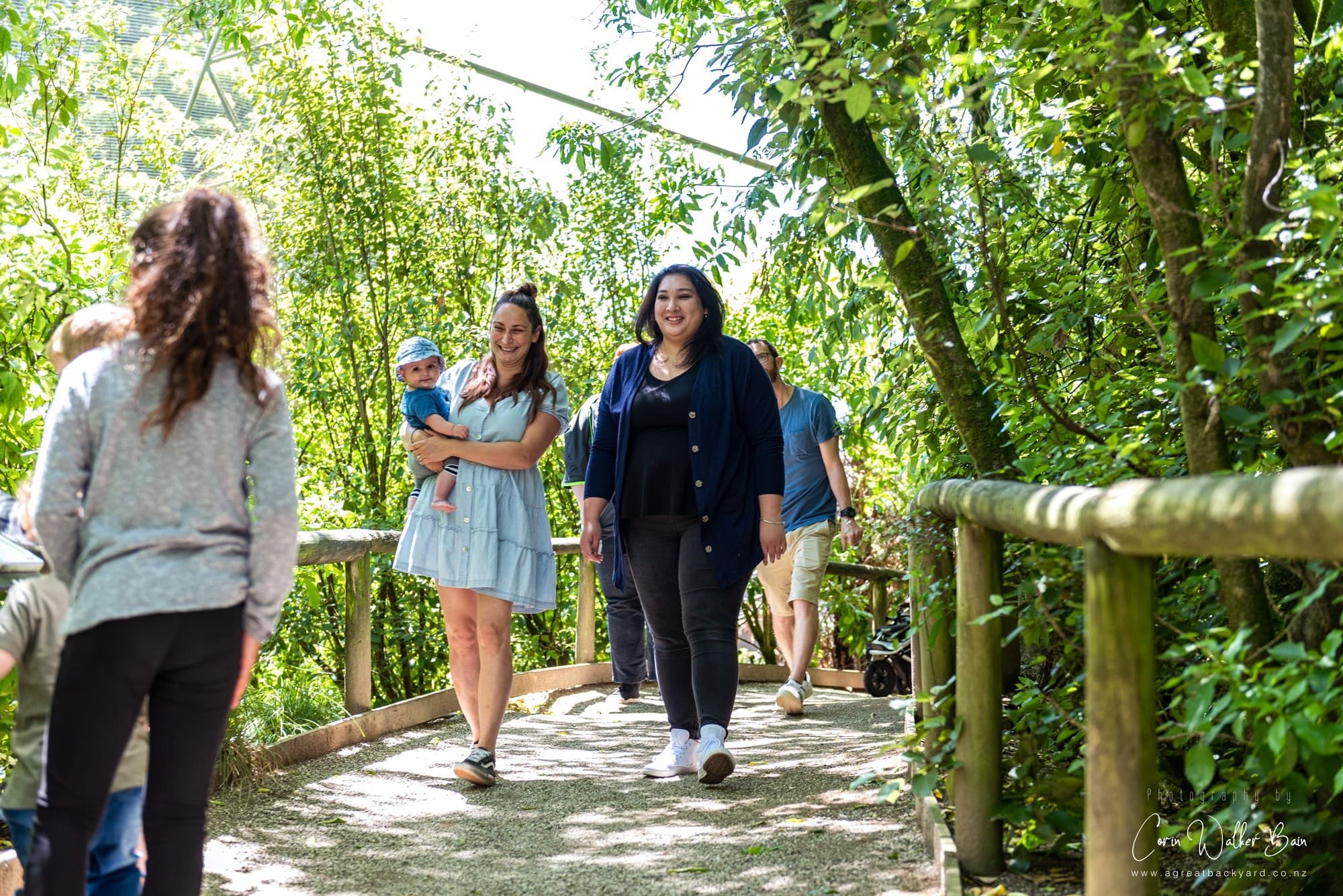 Visitors strolling shaded boardwalk through lush forest garden