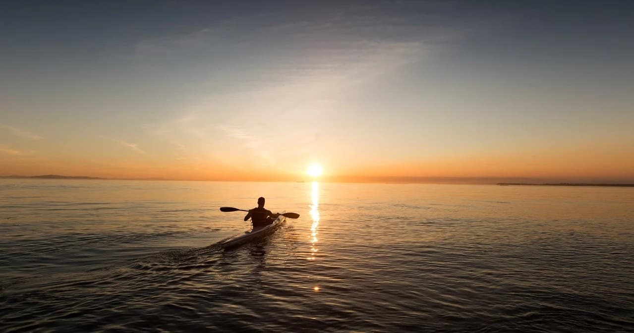 Solo kayaker paddling at sunset on calm open ocean