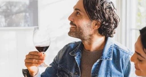 Person sipping red wine indoors with bright window light