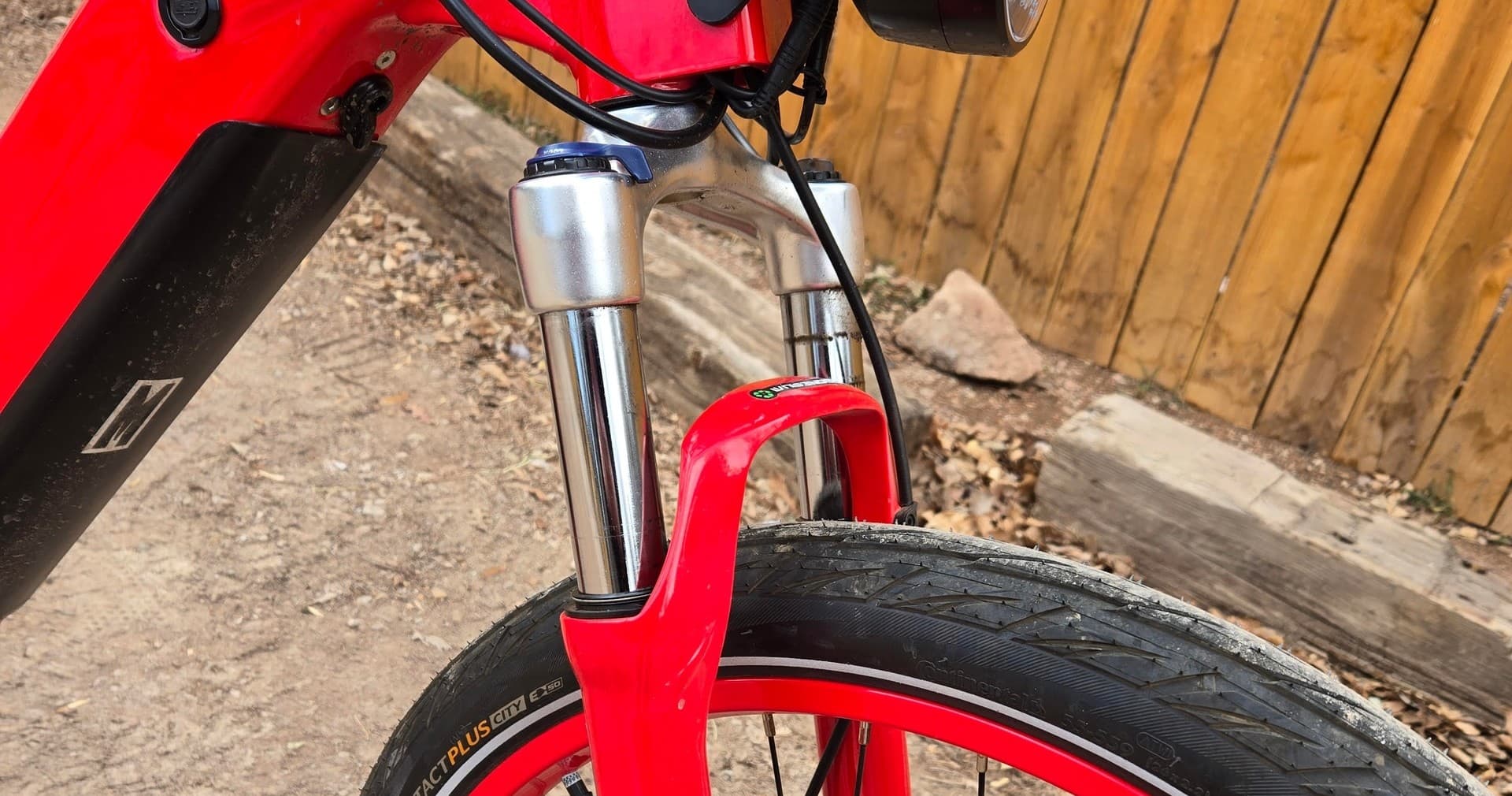 Close-up of red e-bike front fork and tire by wooden fence