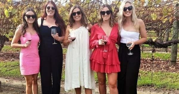 Group of women posing with wine glasses among vineyard rows