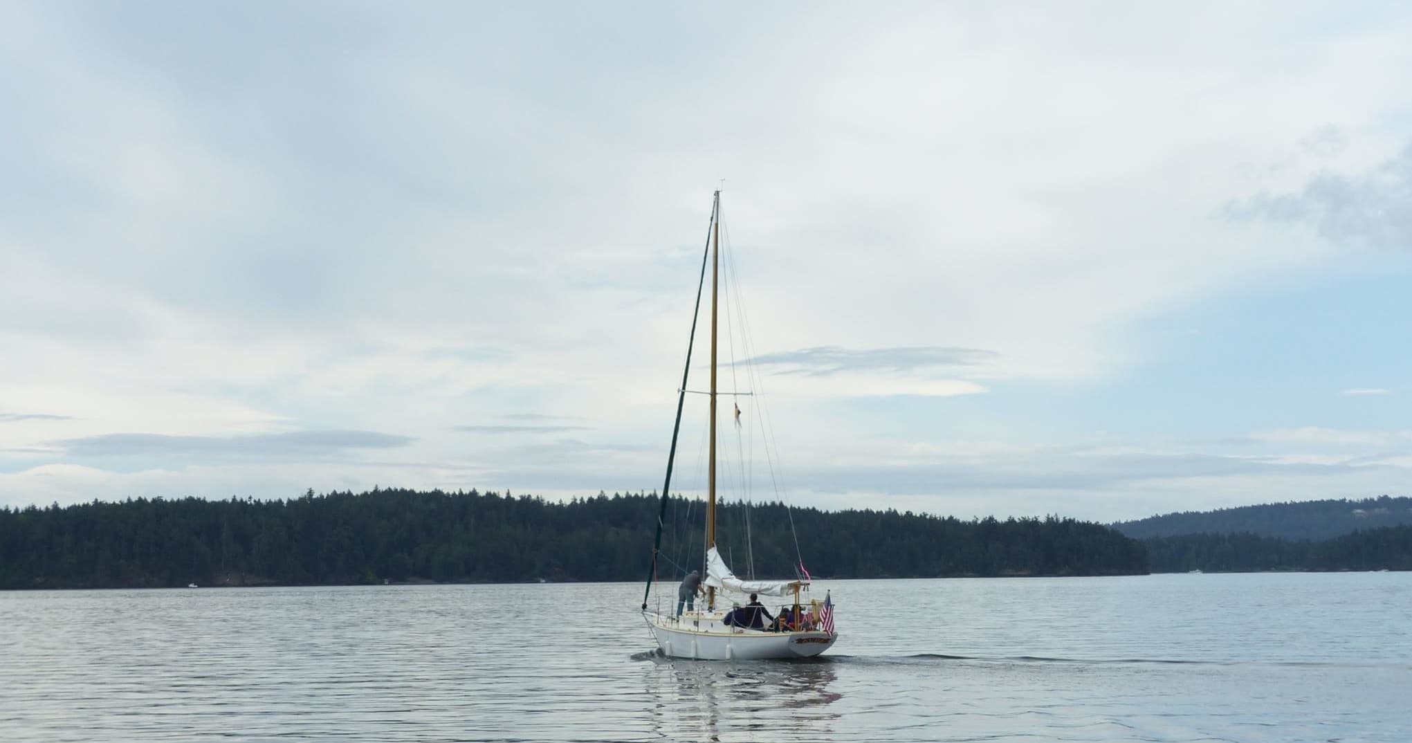 Sailboat on calm open water beneath cloudy sky and treeline