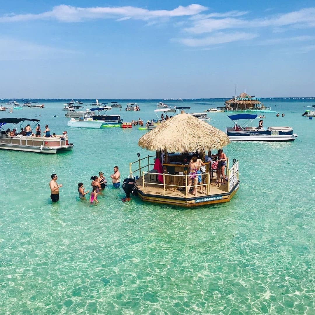Guests wading around floating tiki bar in clear shallow water