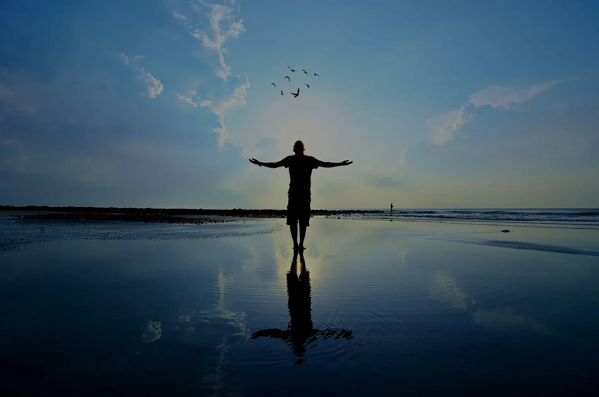 Silhouetted person embracing sunrise reflected on wet beach shore