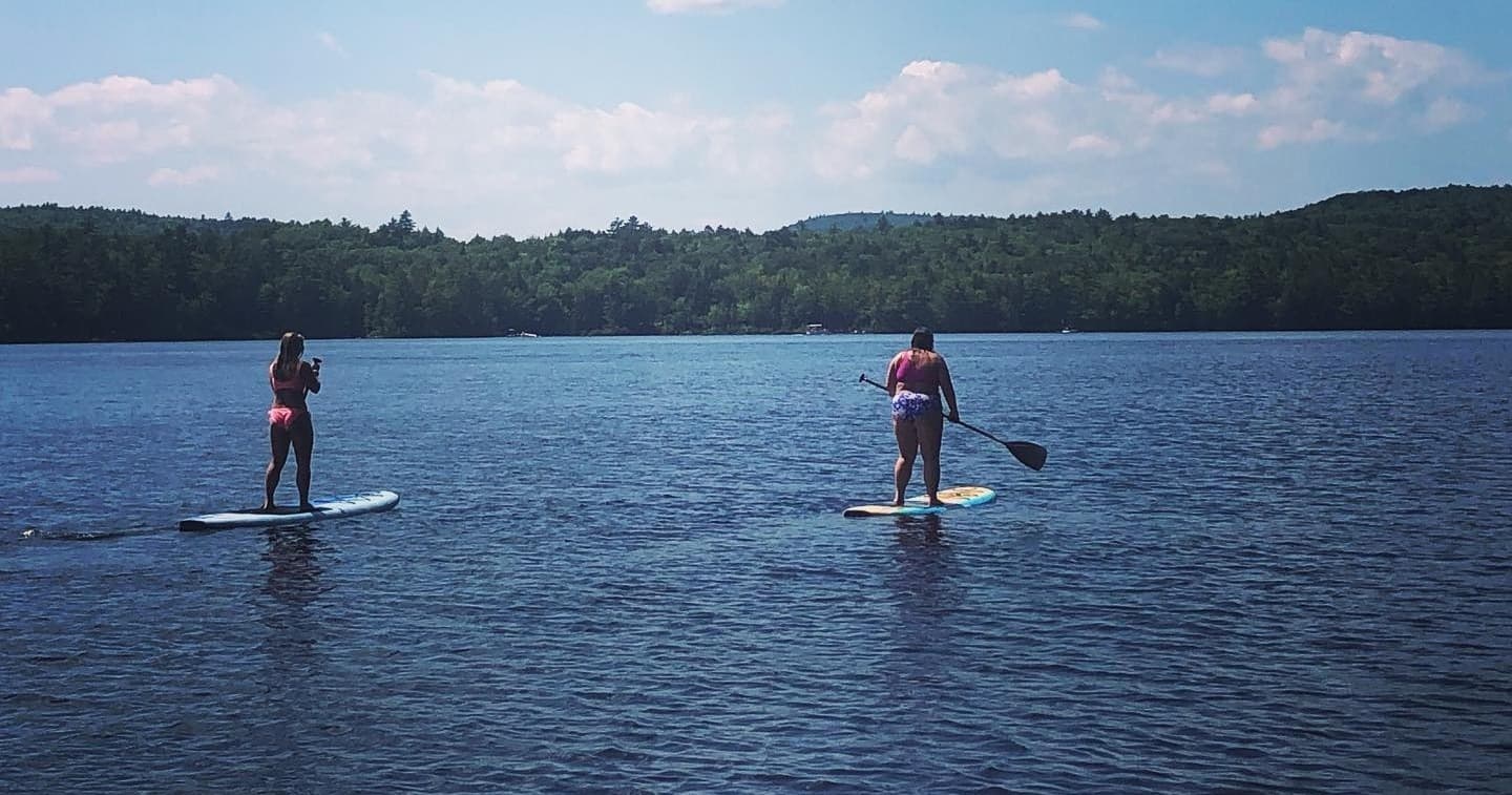 Two paddleboarders gliding across tranquil lake at dusk