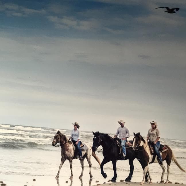 Group of riders trotting along surf line on wide coastal beach