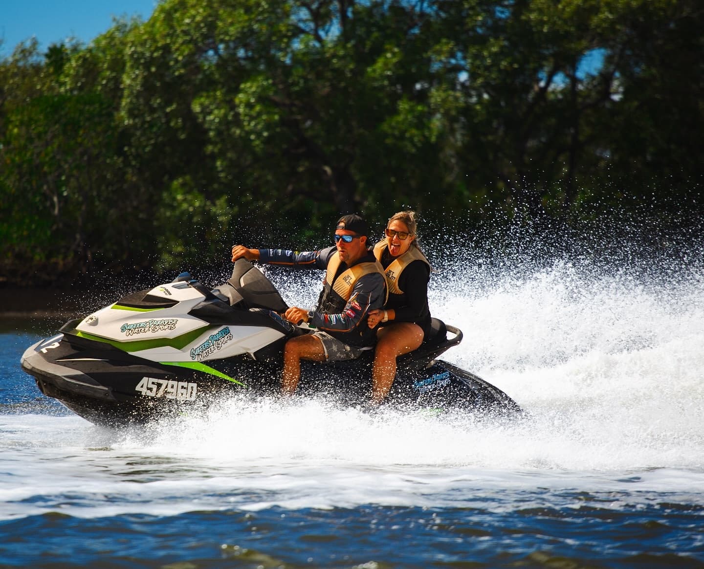 Two riders on jetski speeding past green mangrove shoreline