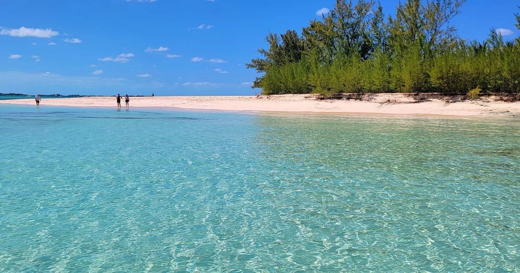 People wading around tropical sandbar in turquoise lagoon