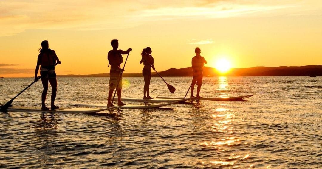 Stand-up paddleboarders silhouetted at sunset on open ocean
