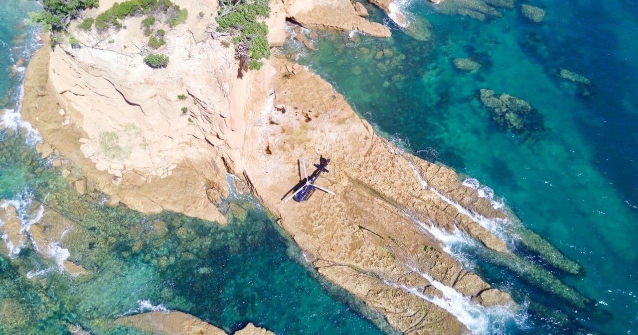 Aerial coastline with swimmer on rocky outcrop, sea views