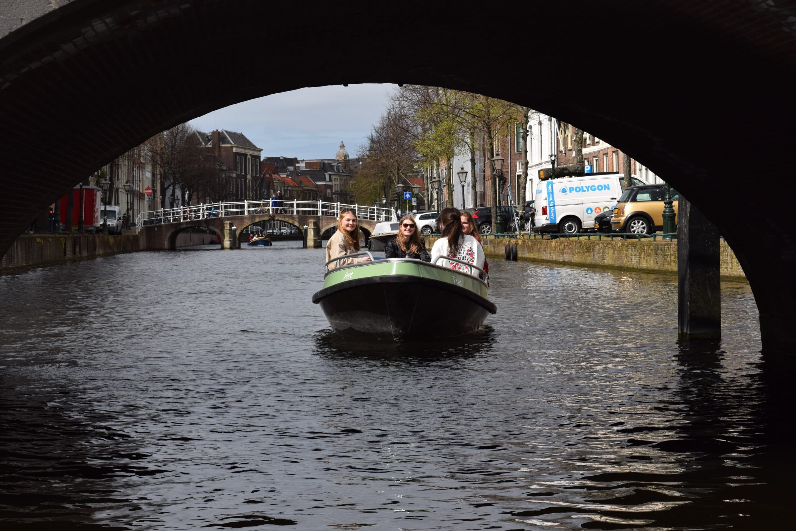 Small tour boat passing under brick bridge in Leiden canal