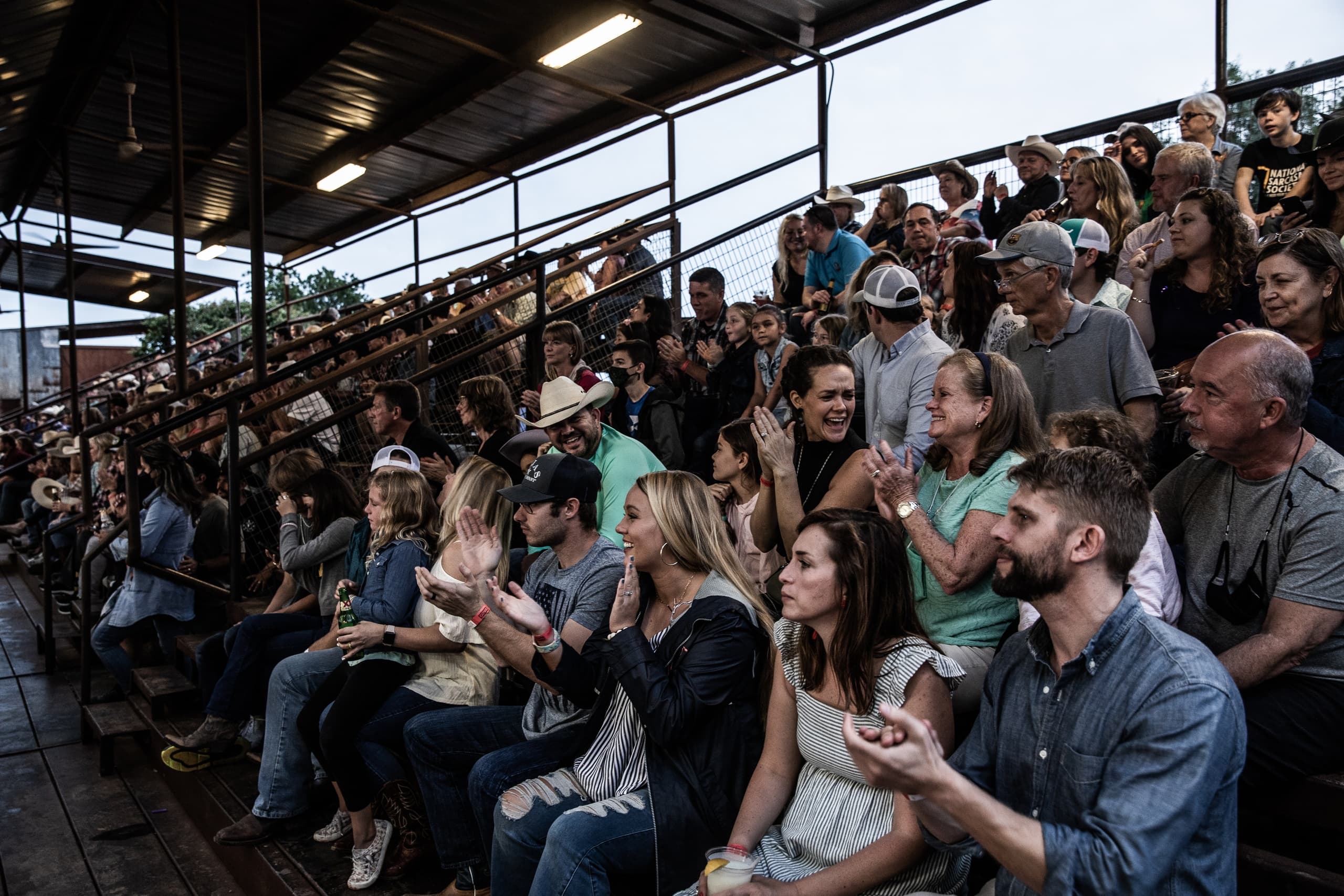 Spectators in covered rodeo grandstands watching outdoor event