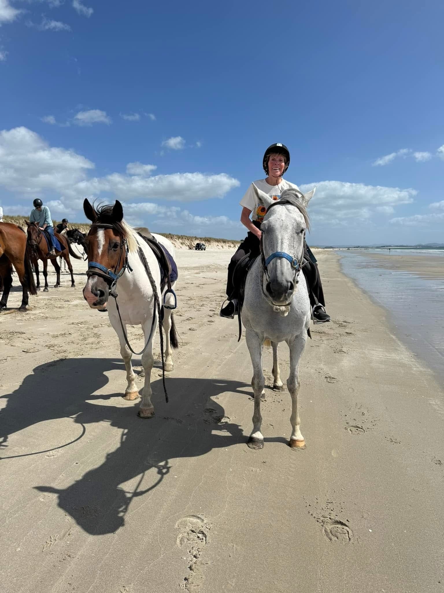 Two riders leading horses on sunlit sandy beach