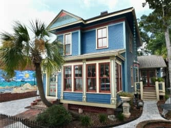 Blue Victorian coastal house with palm trees on sunny street