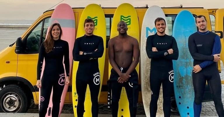 Surf lesson group with colorful boards by beachfront van at shore
