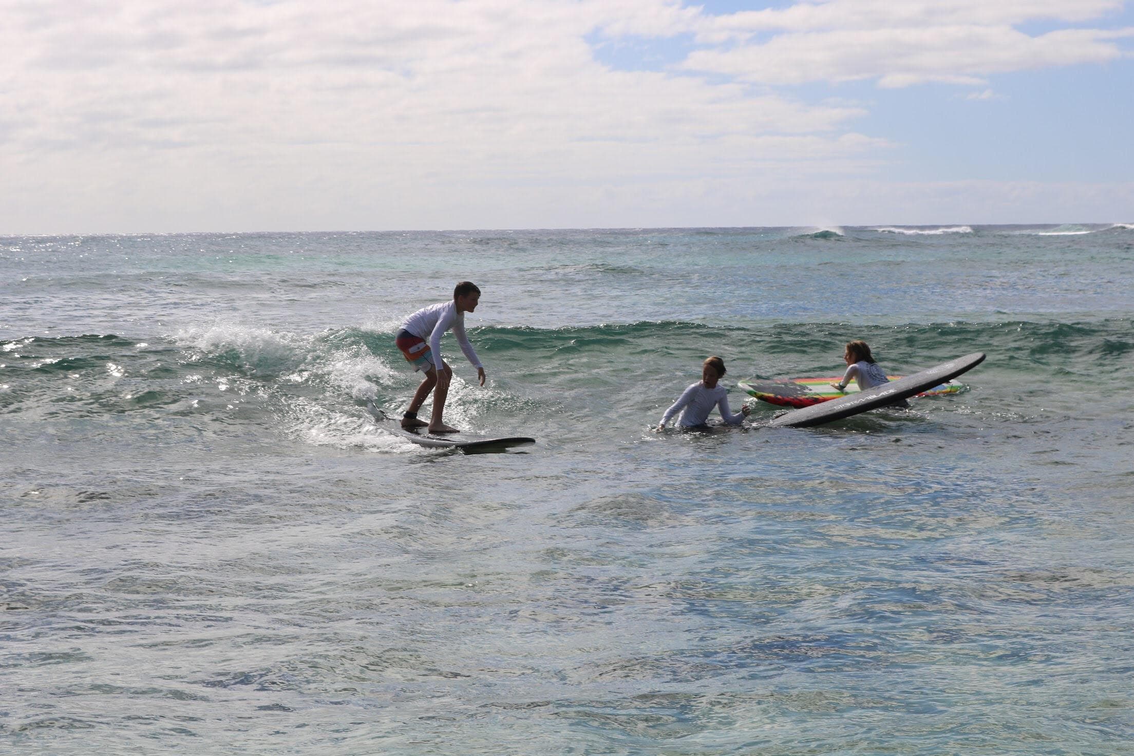Surfers catching small waves near rocky reef off Kauai coast