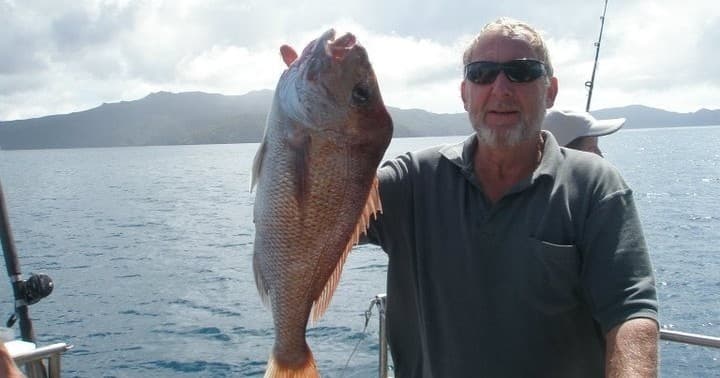 Angler holding large caught snapper aboard sportfishing boat at sea