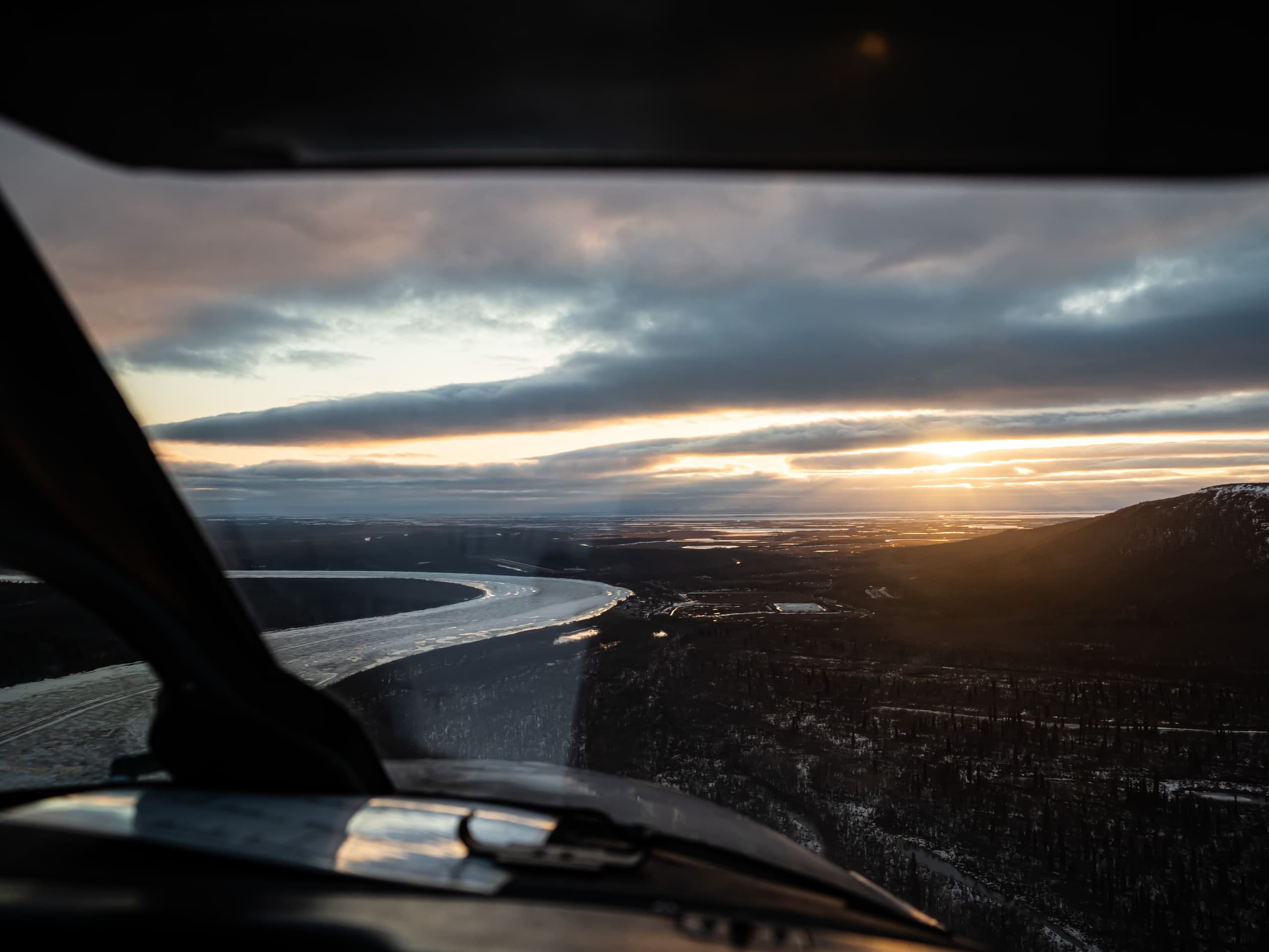 Cockpit view over winding river and sunset across Alaska landscape