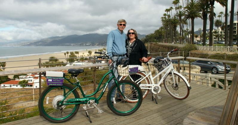Couple posing with cruiser bikes on coastal boardwalk, ocean view