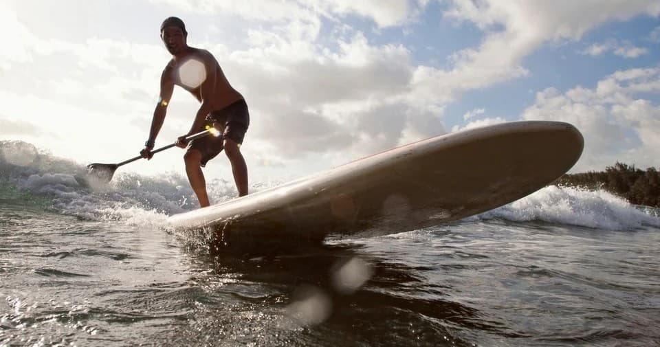 Standup surfer riding breaking wave at sunrise, powerful silhouette