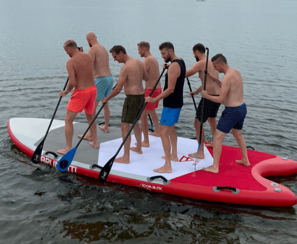 Group stand-up paddleboarding together on calm lake near shore