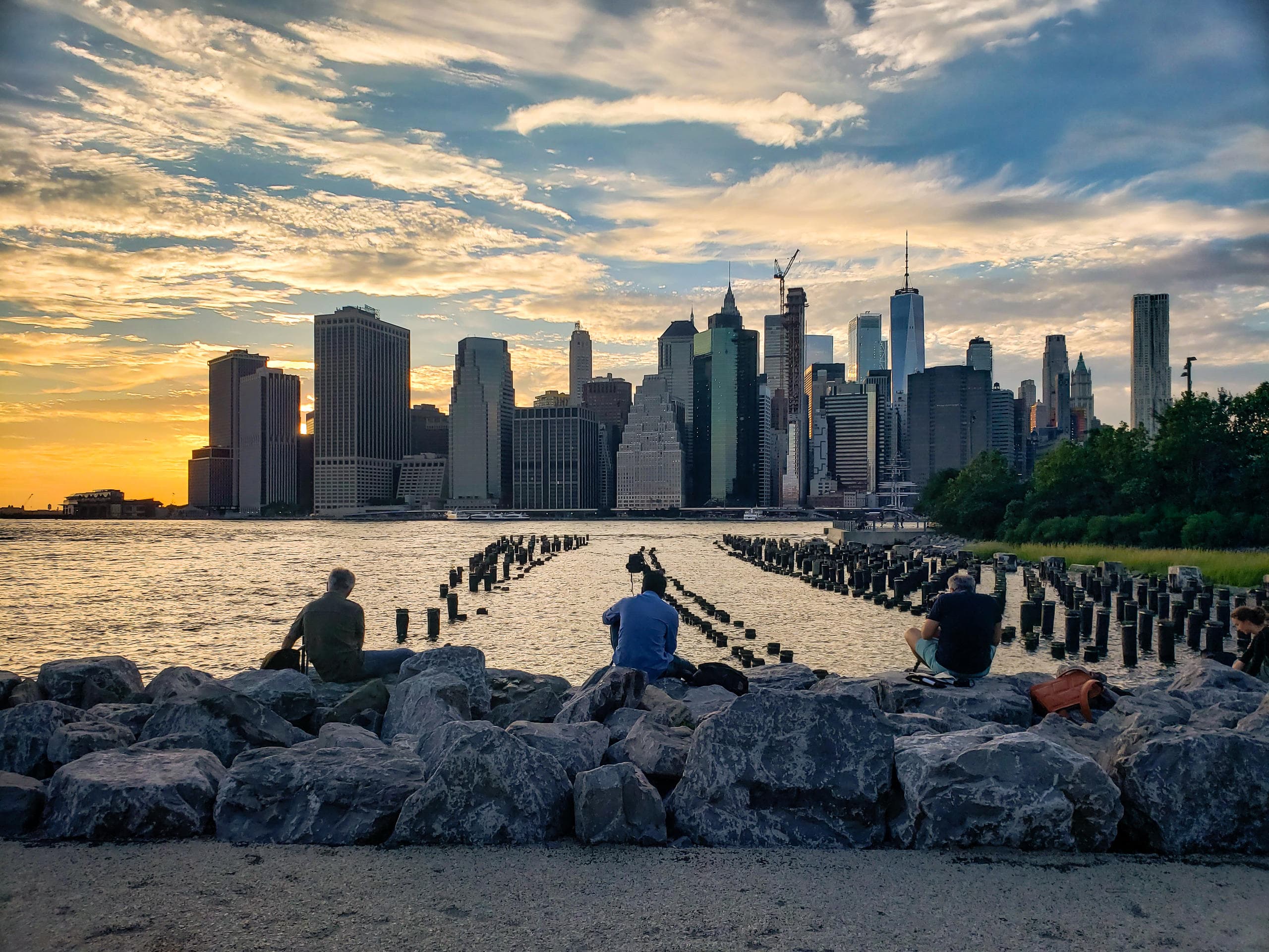 Sunset skyline view over river with people on rocky waterfront