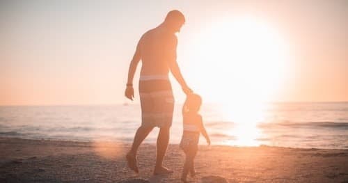 Parent and child walking on beach at sunset, family silhouette