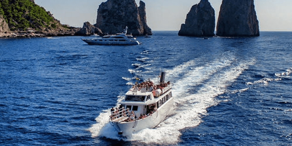 Tour boat speeding past Capri rock arches through turquoise sea