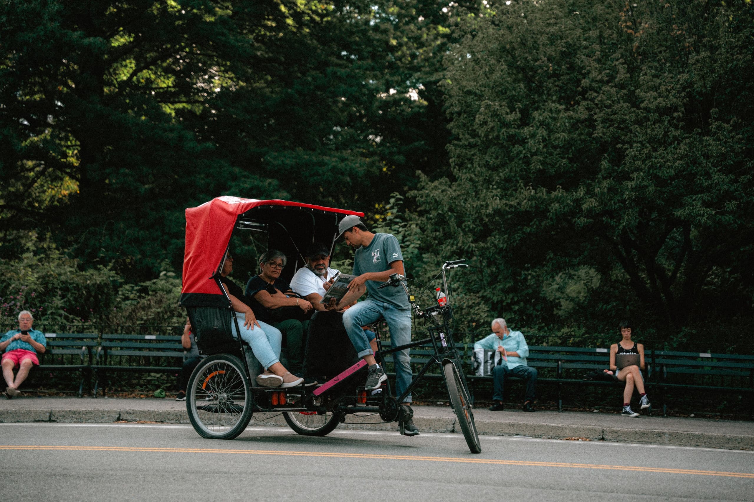Red-canopied pedicab on road with passengers in park setting