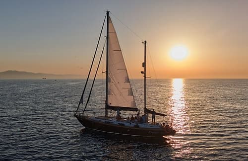 Sailboat cruising at sunset on open ocean with coastline