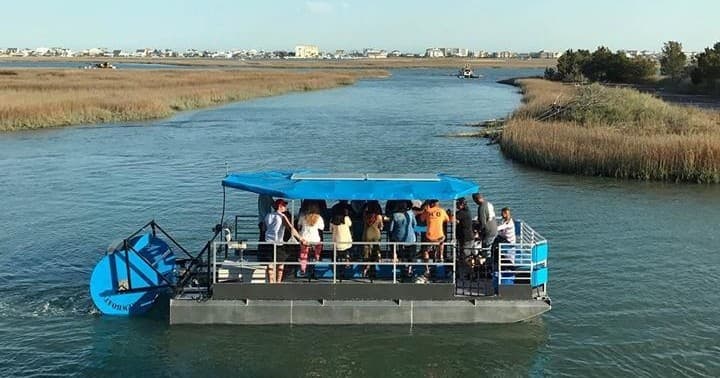 Passenger paddleboat cruising marsh channel through tidal estuary