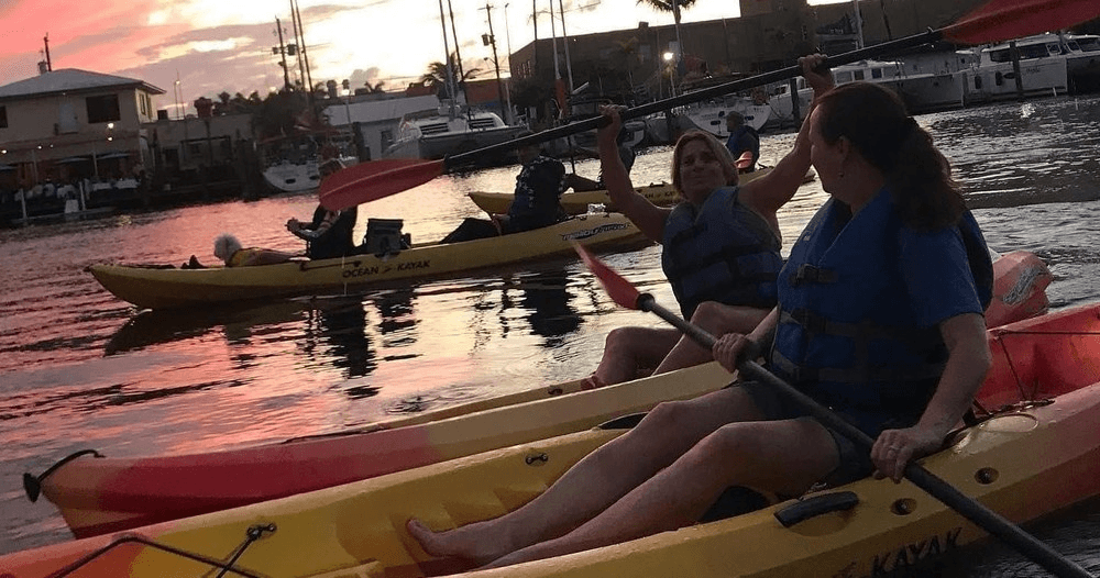 Kayakers paddling at sunset through canal lined with palm trees