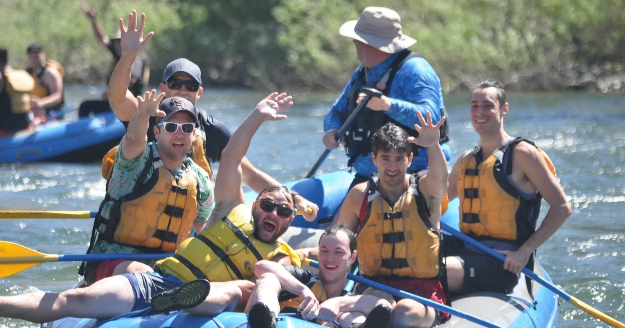 Group whitewater rafting on sunny river, paddling and cheering
