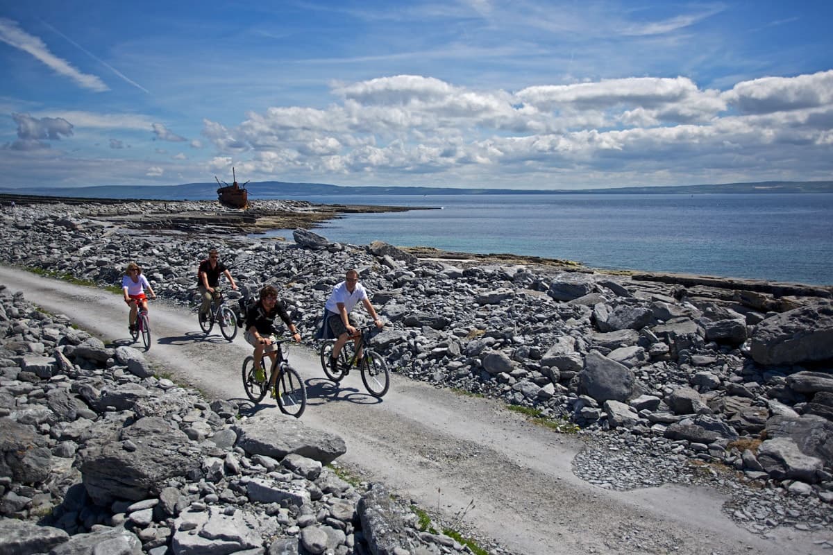 Cyclists biking along rocky coastal trail under blue sky