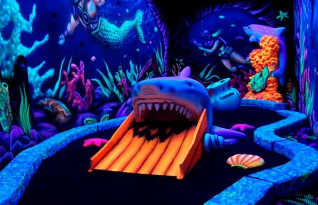Glow-in-the-dark indoor mini golf with shark mouth obstacle
