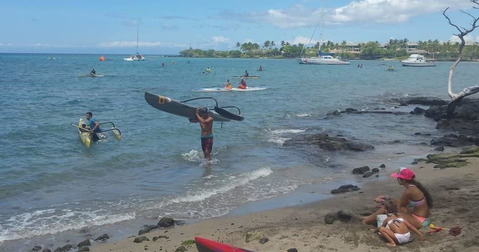 Surfer carrying board along crowded sandy beach near reef
