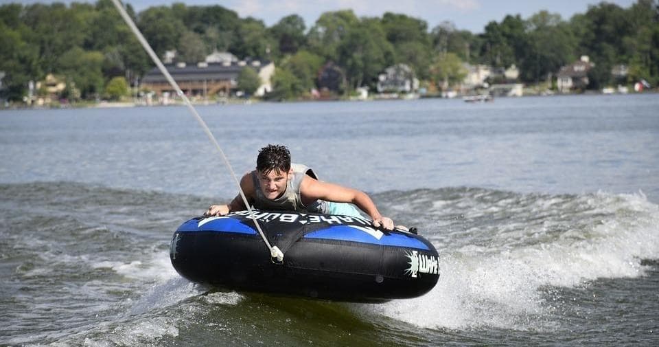 Person tubing behind boat across choppy recreational lake