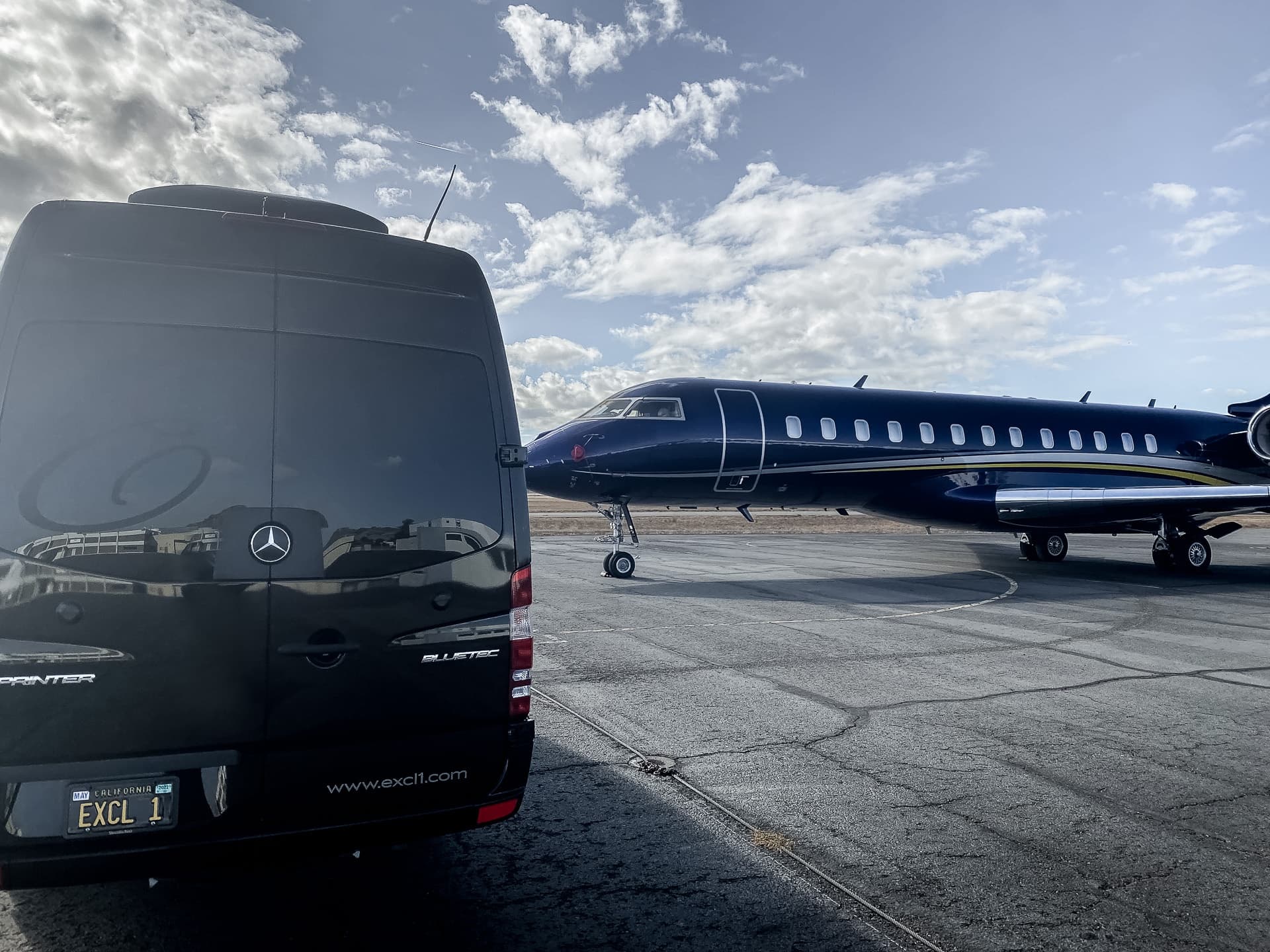 Black shuttle van parked beside private jet on sunny tarmac